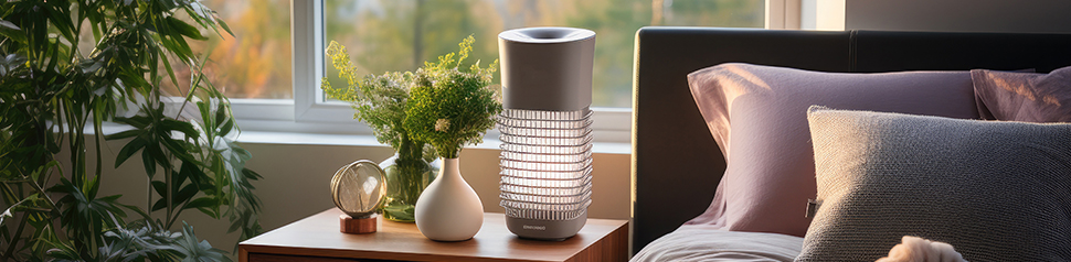 a bedroom with an air purifier on a bedside table with a plant opposite and window behind